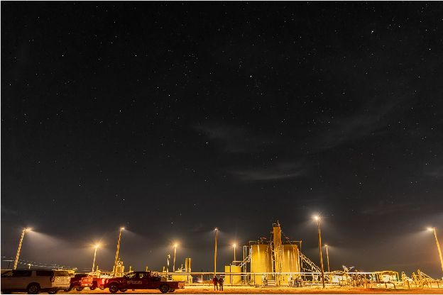 A starry night sky above a downward-lit oil and gas production site