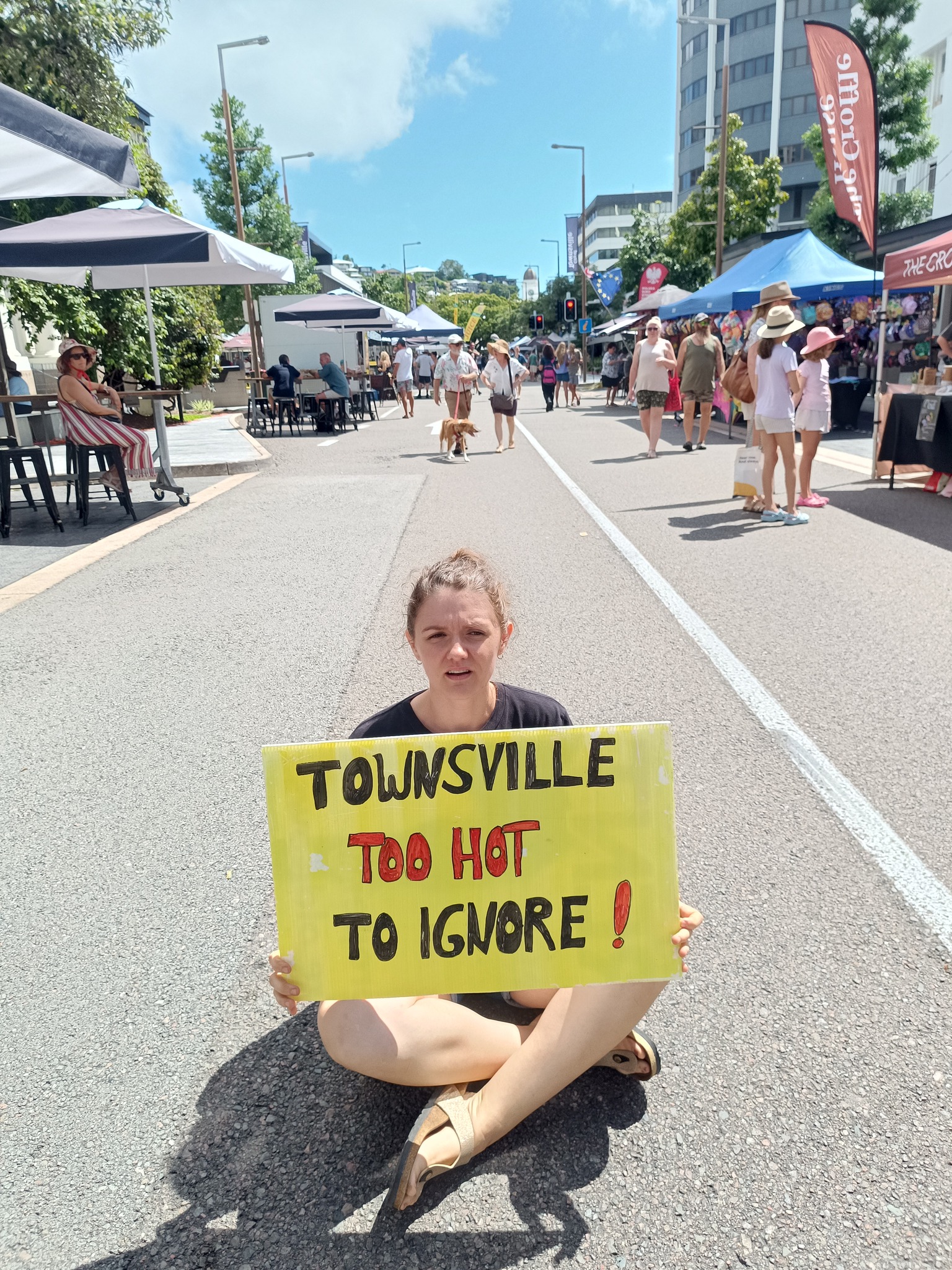 Luna sits on Flinders street with sign that reads "Townsville: too hot to ignore!"