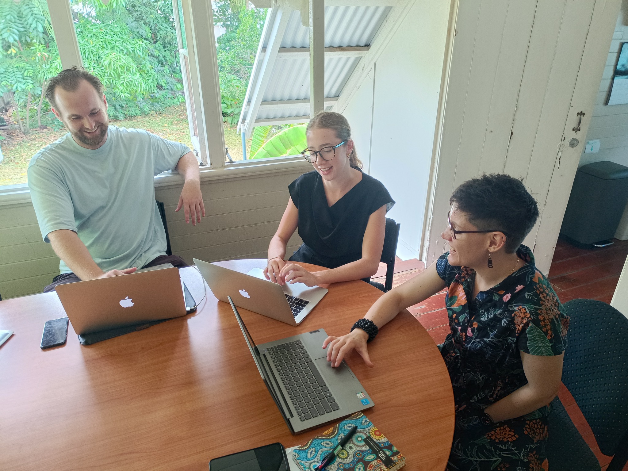 Smiling volunteers work with Crystal at laptop computers around a table