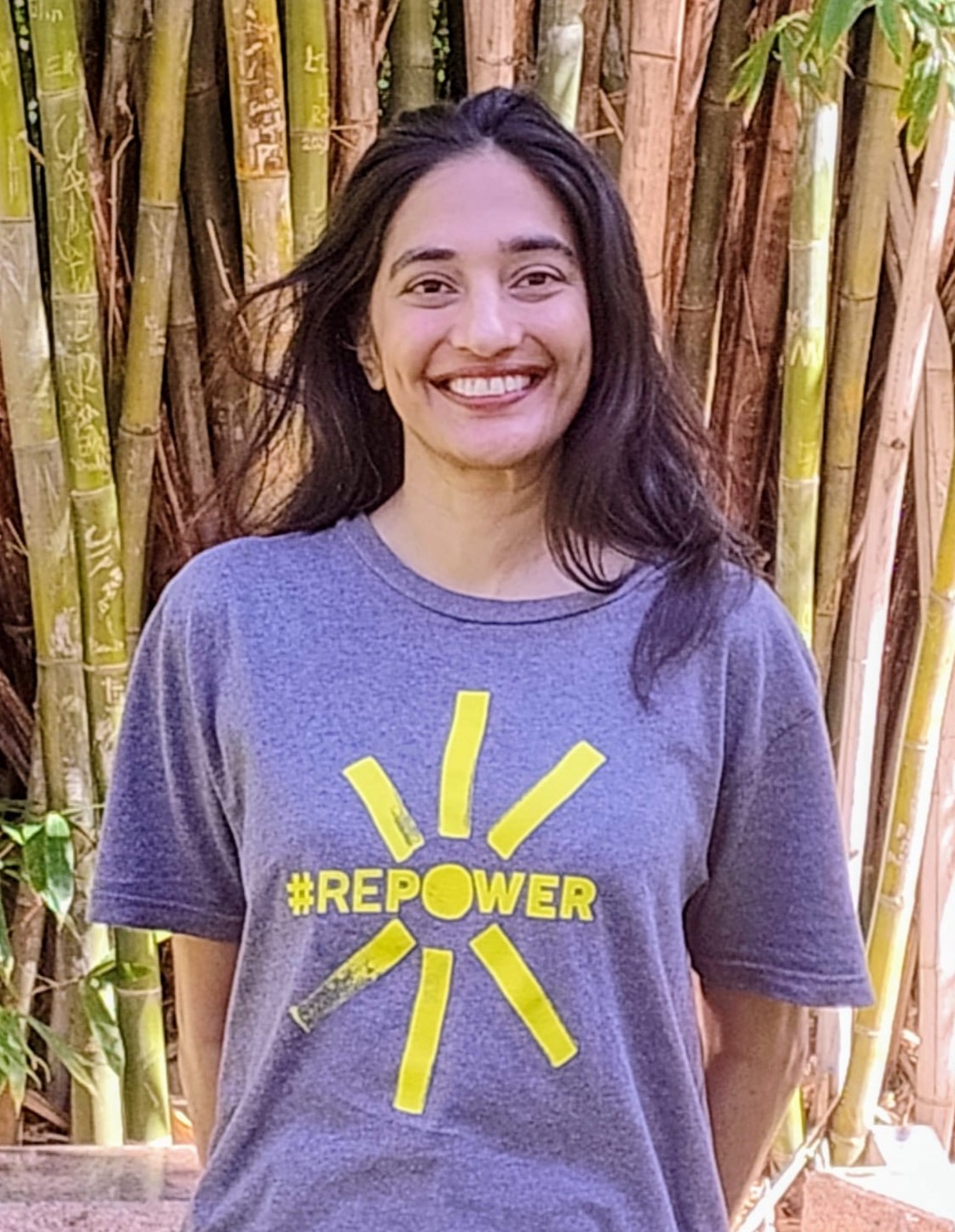 Rooka Price smiles in front of some tall bamboo, wearing a t-shirt that says "Repower"