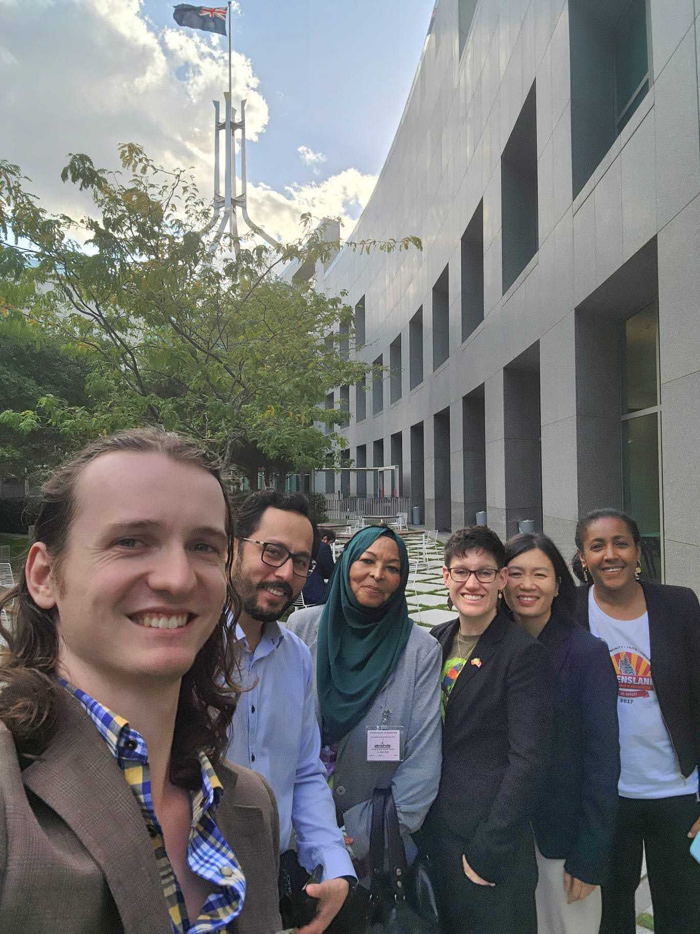 The Queensland delegates stand with the flag on Parliament House in the background