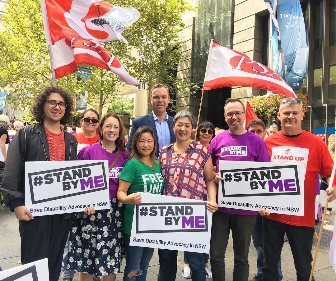 Abigail with a group of people standing in a row with signs that read '#standbyme save disability advocacy in NSW'
