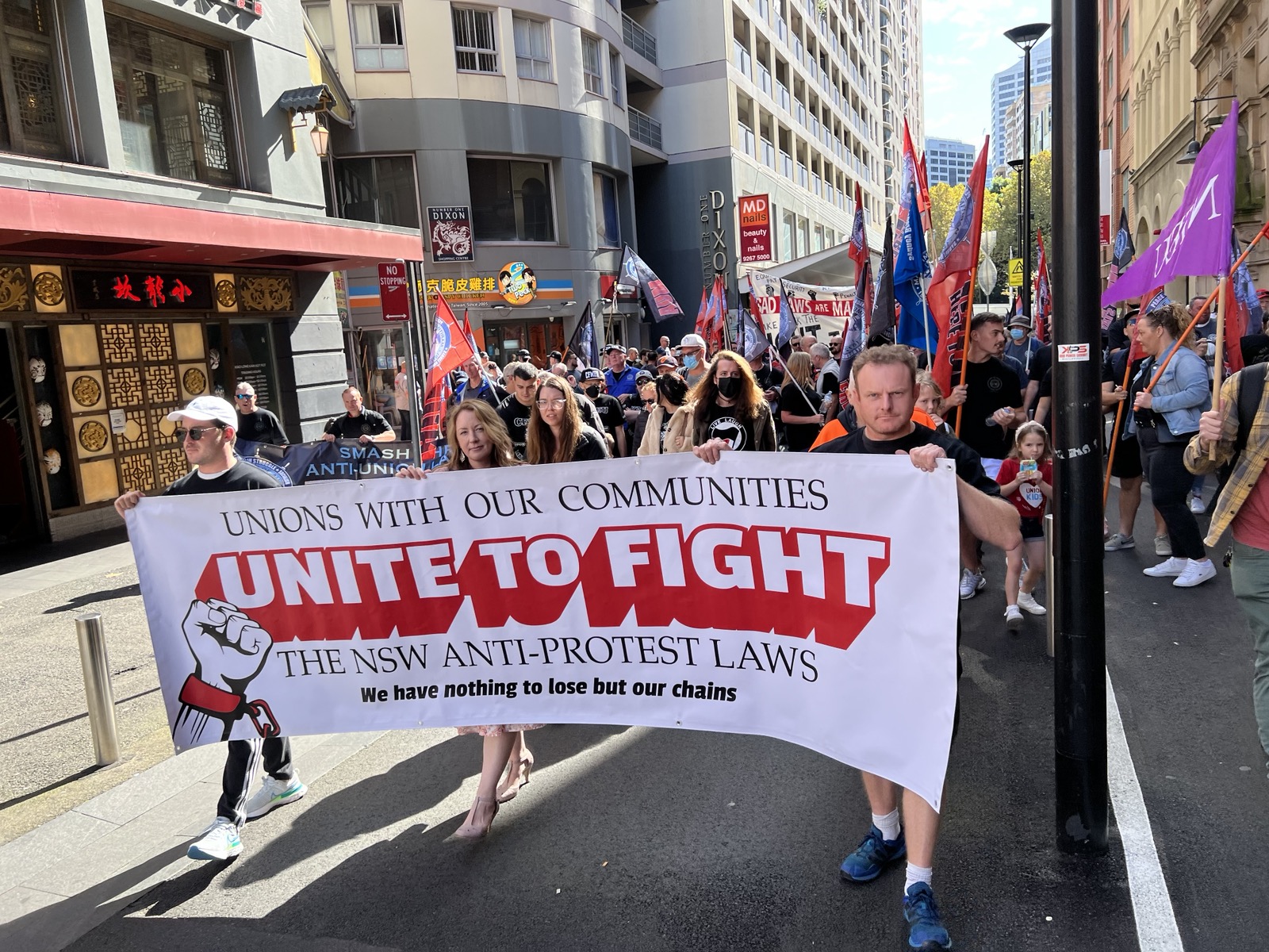 Abigail marching with people in the street behind a banner that reads \