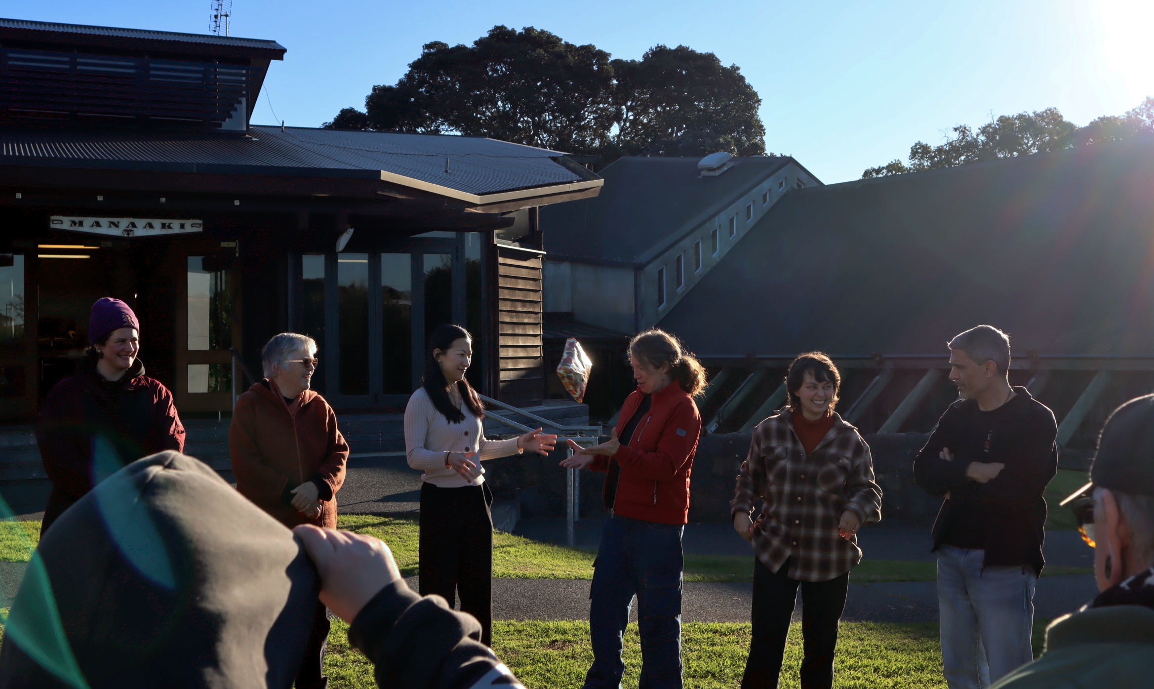 OraTaiao members play pass the parcel outside in the sun.