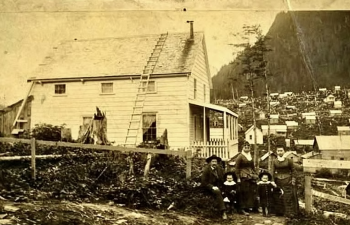 Richard Tighe Harris and his family in front of their home on Courthouse Hill in Juneau in 1889. The land appears newly cleared; tree stumps are visible beside the house. (Alaska State Library and Historical Collections)