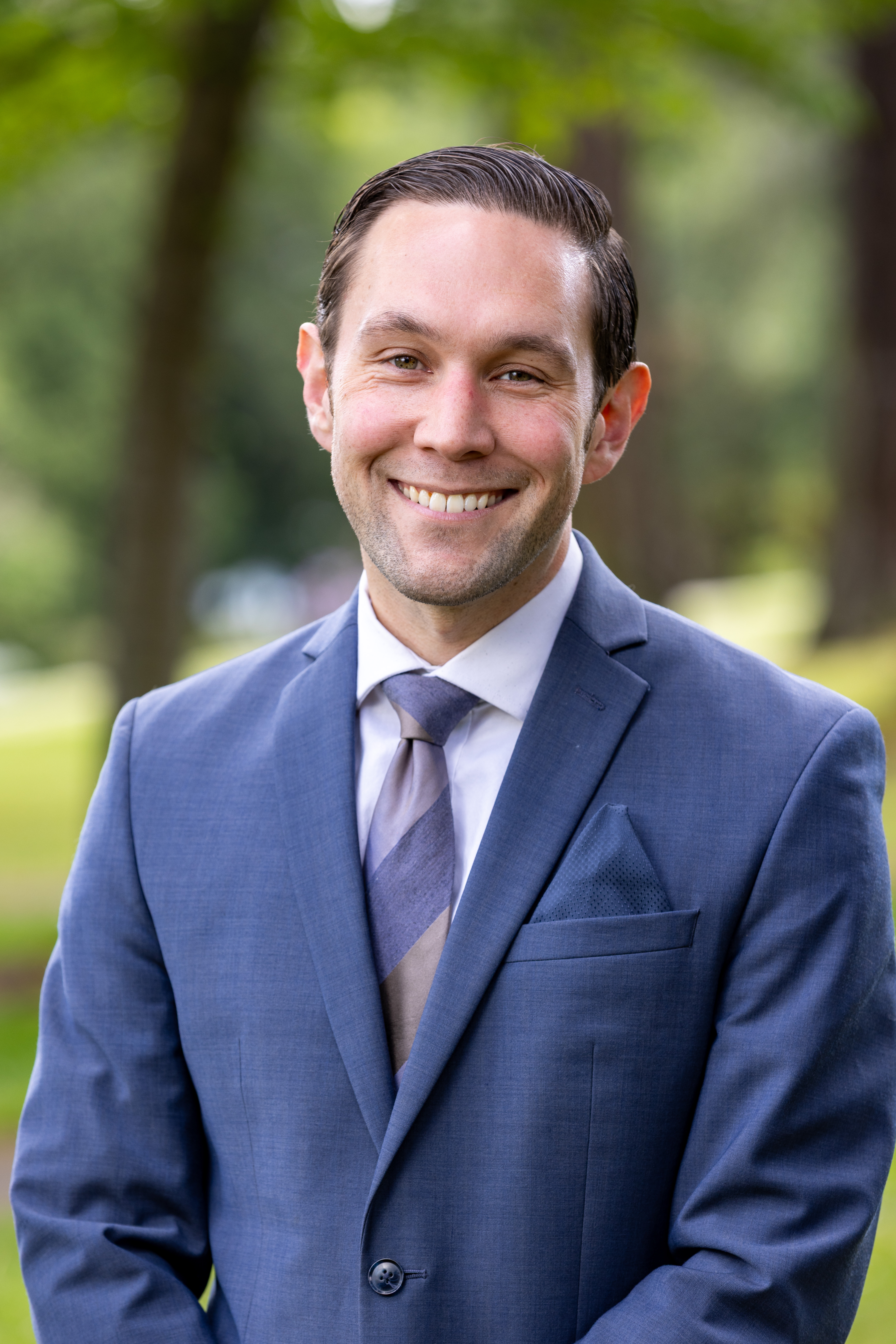 Portrait of Ryan McIrvin smiling wearing jacket and tie.