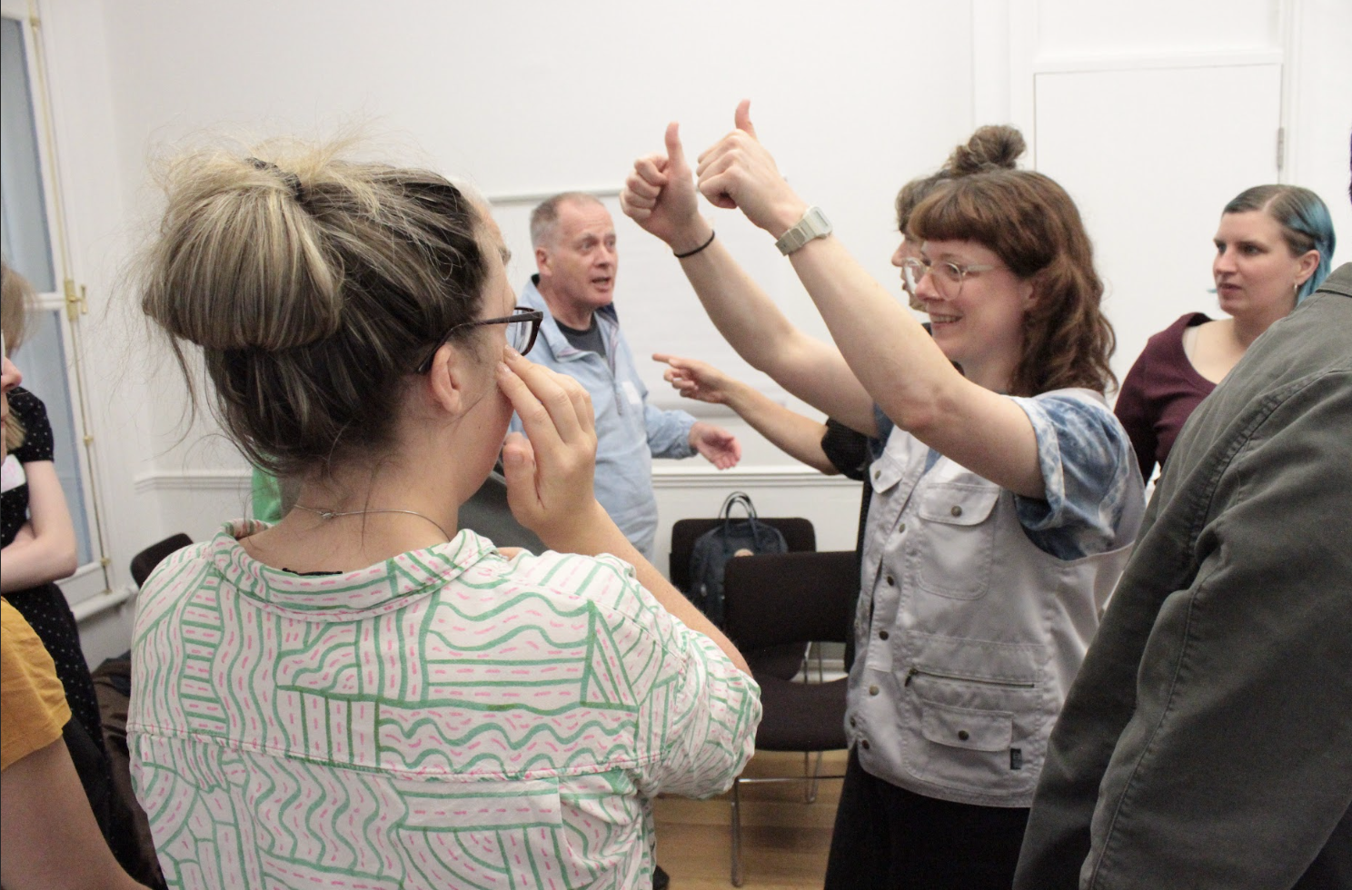 People standing taking to one another. One person is holding their arms up and putting two thumbs up