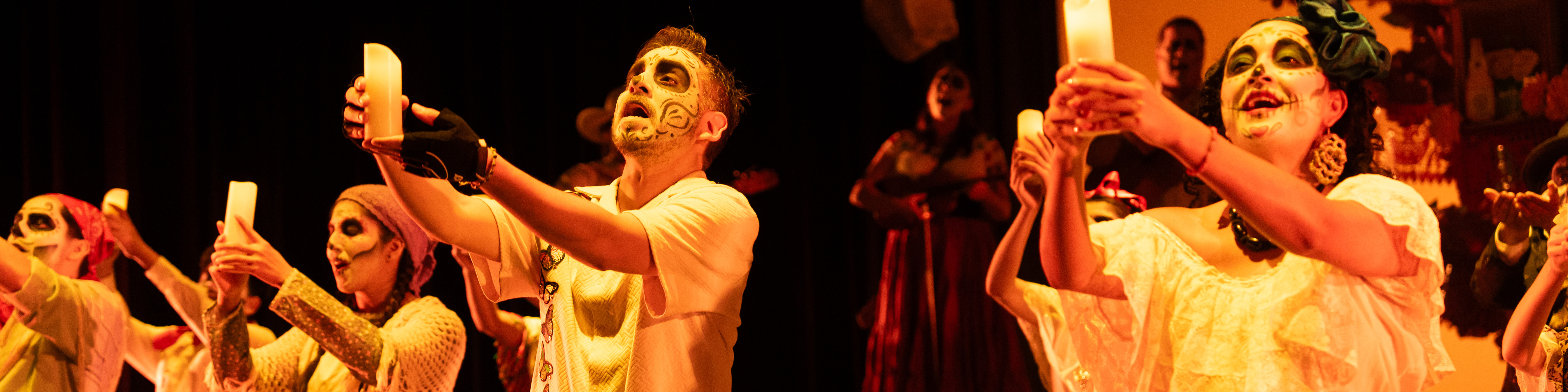 Actors in calavera-style makeup holding candles aloft.