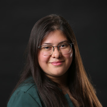 Headshot of Dyana Aguilera, with long brown hair, glasses, and a green blazer.