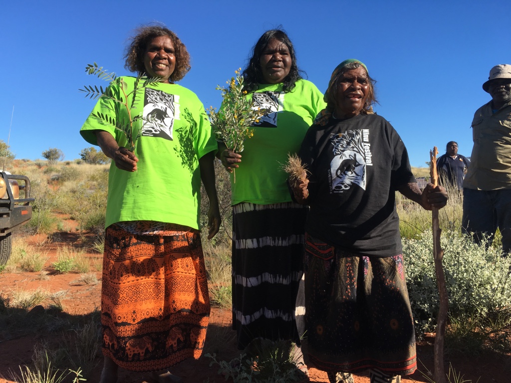 Kiwirrkurra_rangers_Sally_Butler__Monica_Jurrah__Josephine_Nungala_show_festival_attendees_plants_associated_with_bilby_food_on_country.jpeg