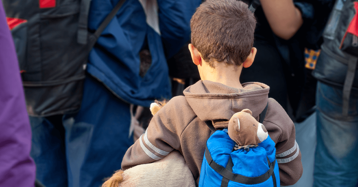 A child refugee with teddy bear in backpack
