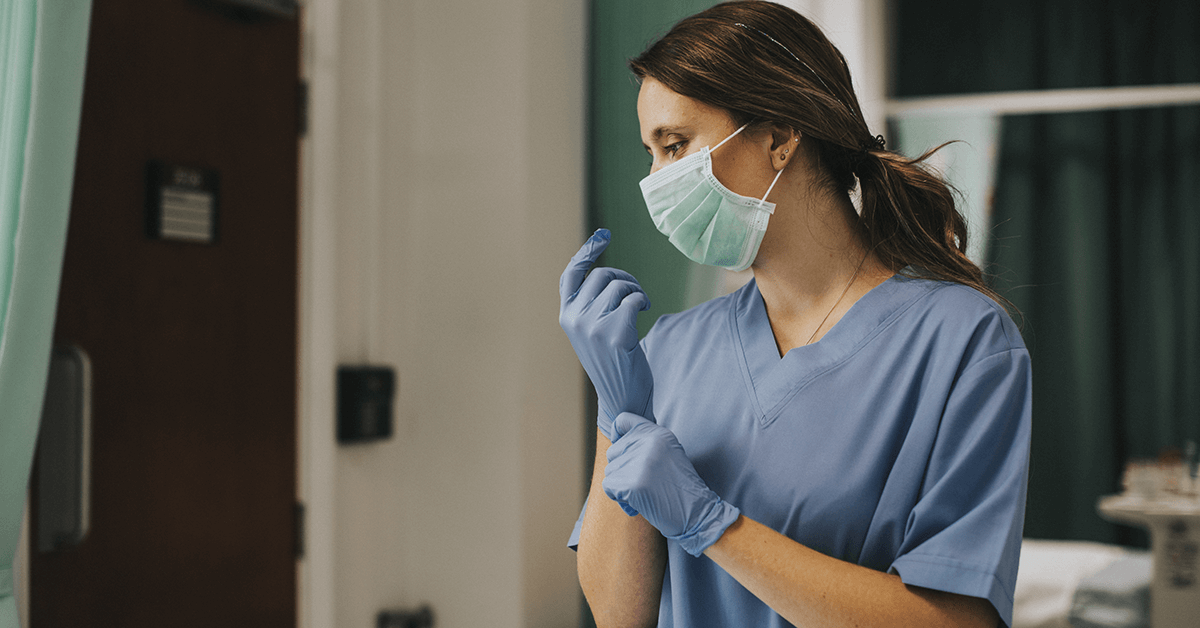 Medic in scrubs and mask pulling on a glove