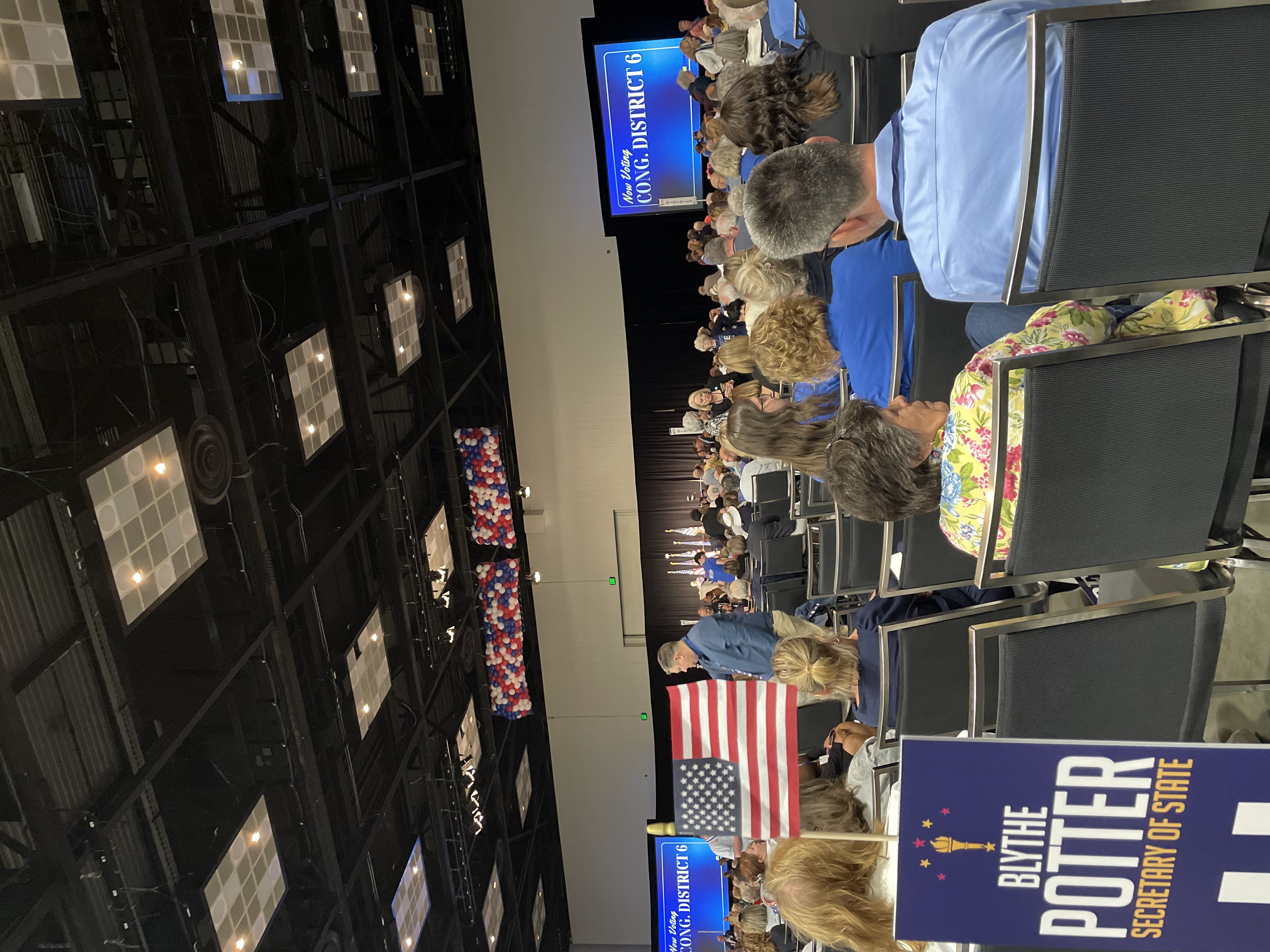 View across the packed convention floor as the screens read Now Voting, Congressional District 6.