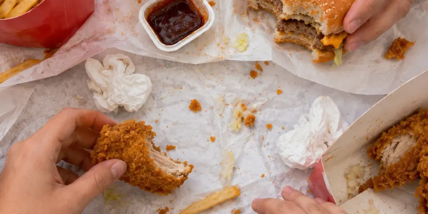 Hands sharing a takeaway fast food meal of fried chicken, burgers and chips