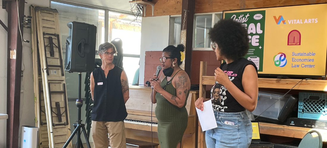 Presenters at our Artist Legal Cafe Three presenters in front of a colorful banner with the logos of the co-hosting events: Vital Arts, Sustainable Economies Law Center, and Movement Law