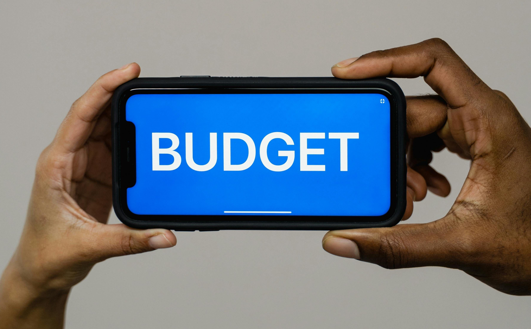Two hands holding a smartphone in landscape mode presenting the word "budget" in capital letters.