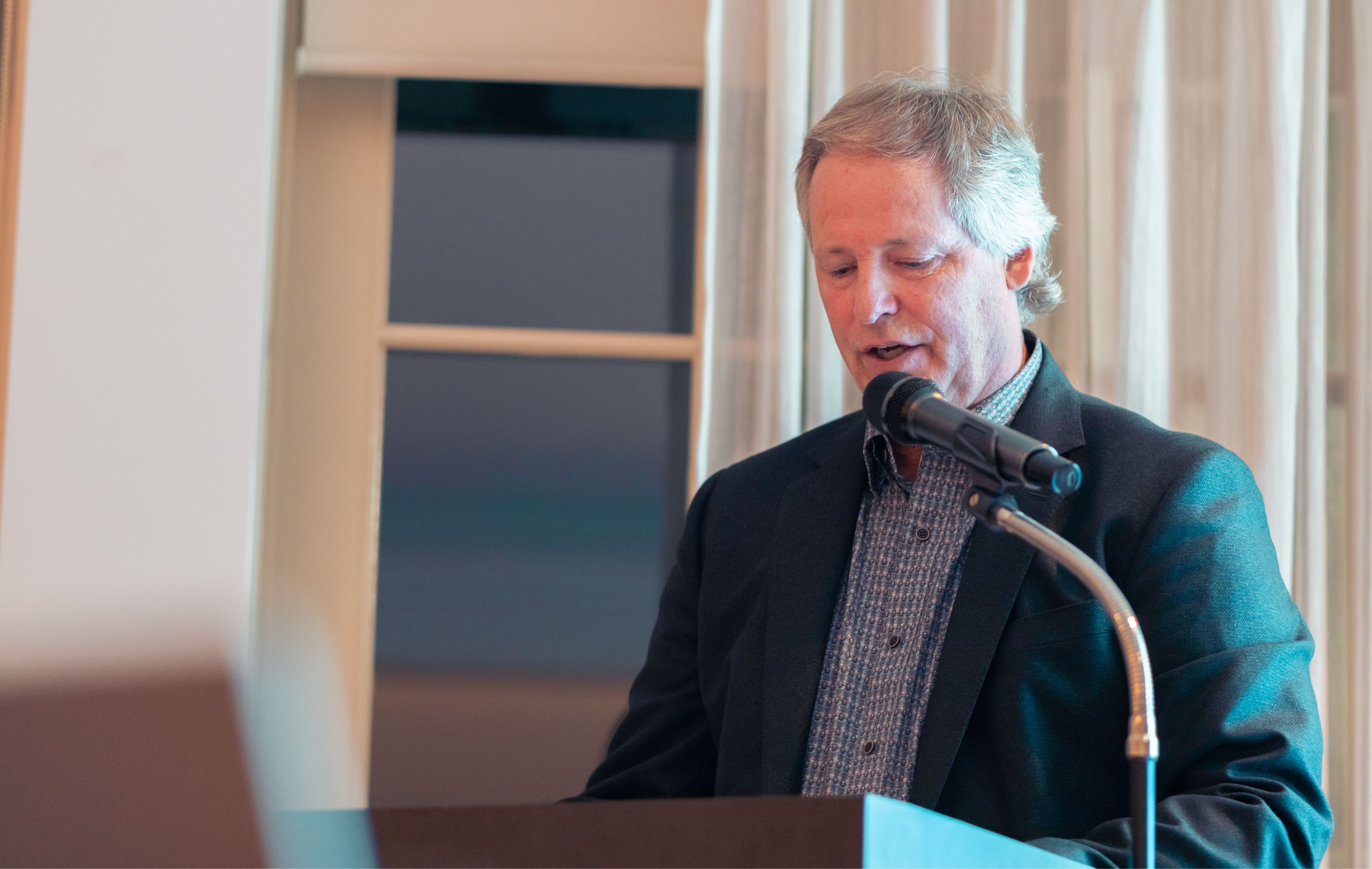 A man with greying hair speaking into a microphone at a podium