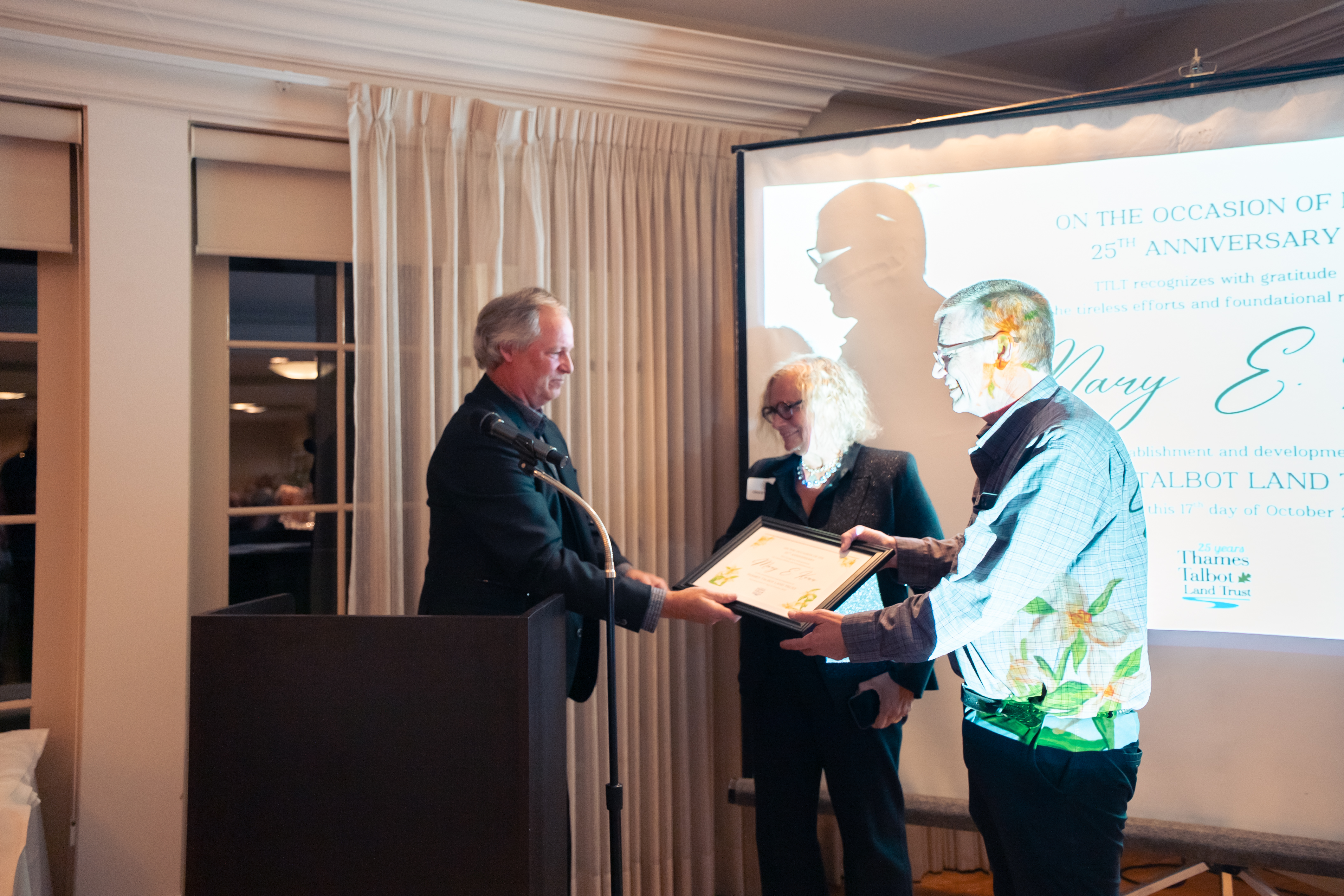 A man and a woman accepting a framed certificate from a man