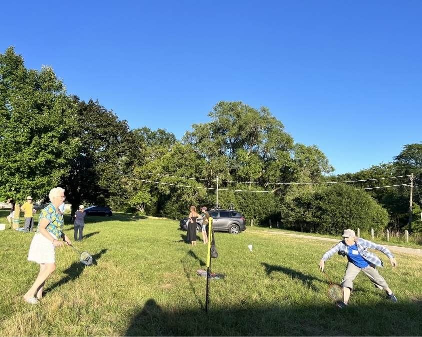 Two women play badminton over a net against each other on green grass