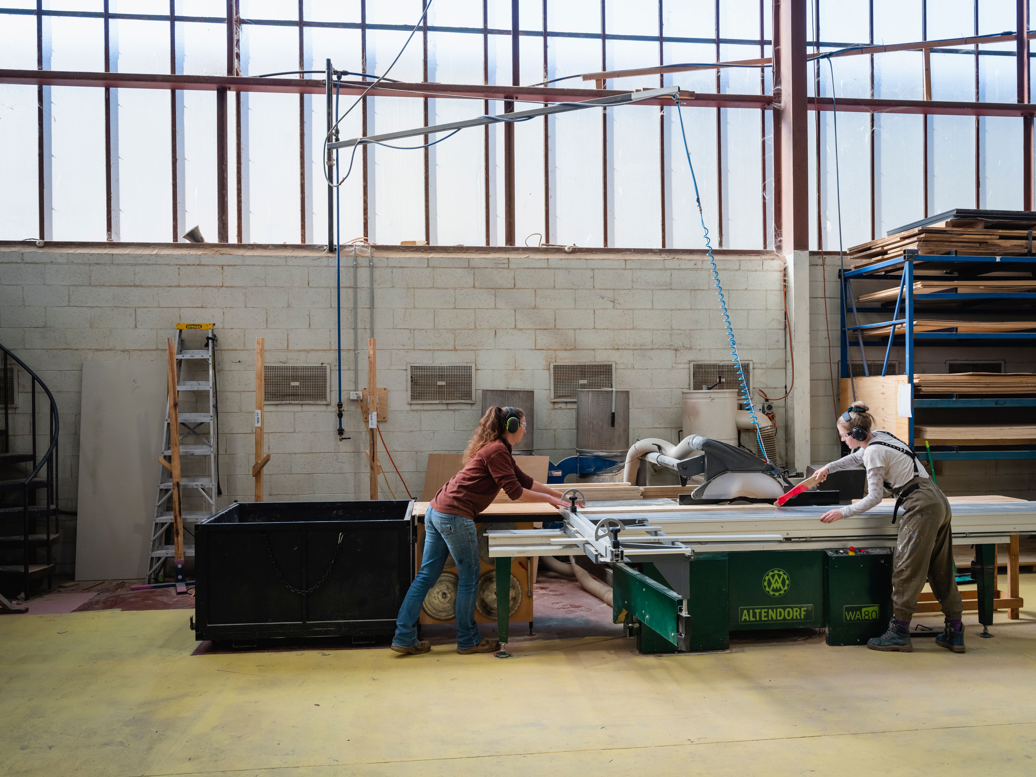 two women operating a table saw together in an industrial setting