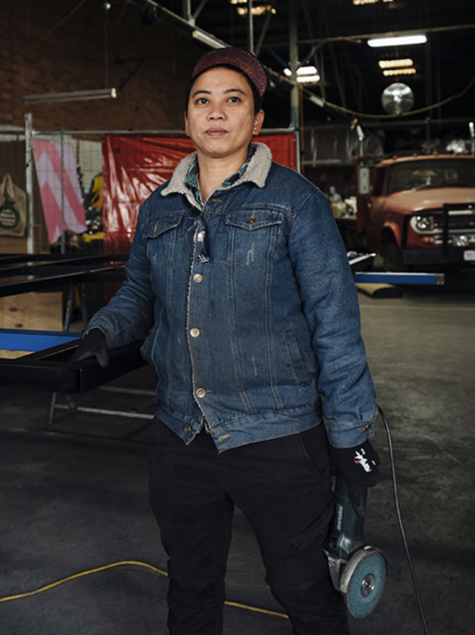 Quelly is holding an angle grinder, standing in a workshop