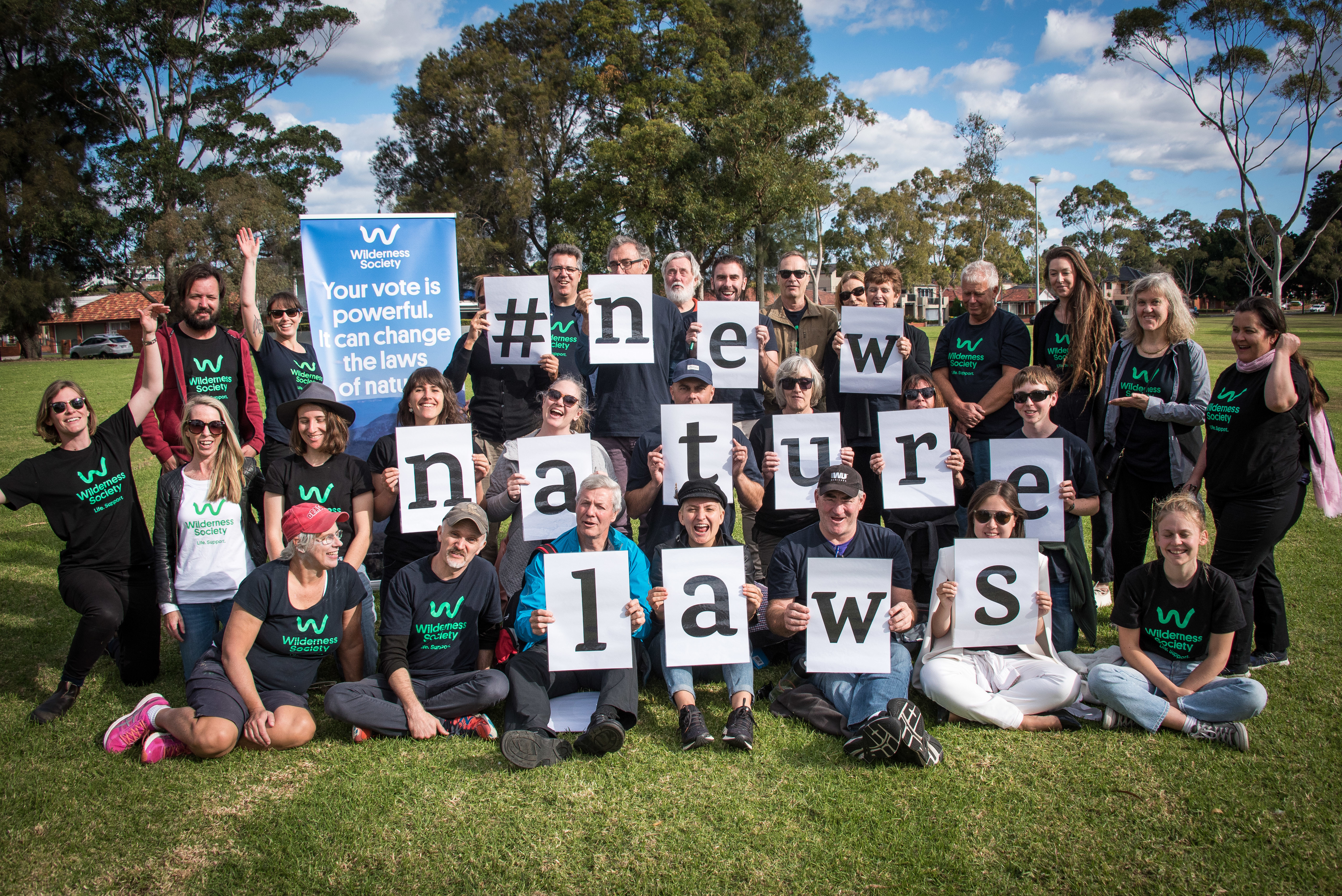 a large group of people outside hold signs spelling out New Nature Laws