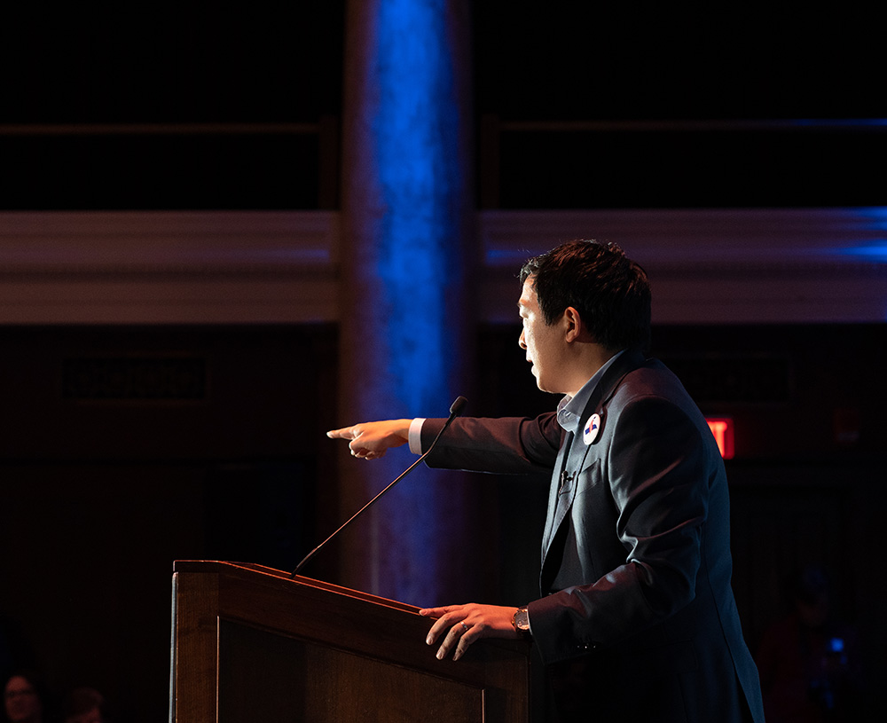 Andrew Yang stands at a lectern and addresses a crowd